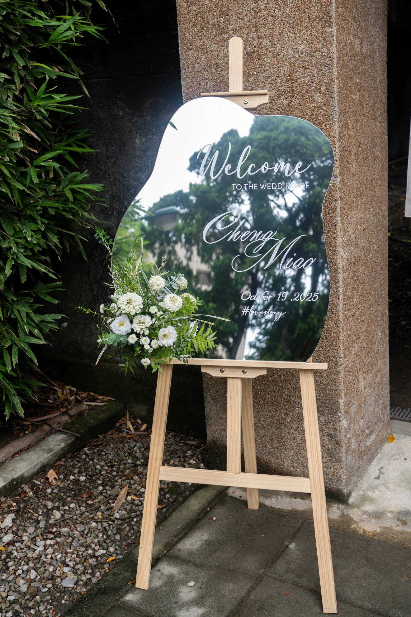 東美園證婚入口的鏡面迎賓牌,搭配白綠小花與竹木庭院背景
