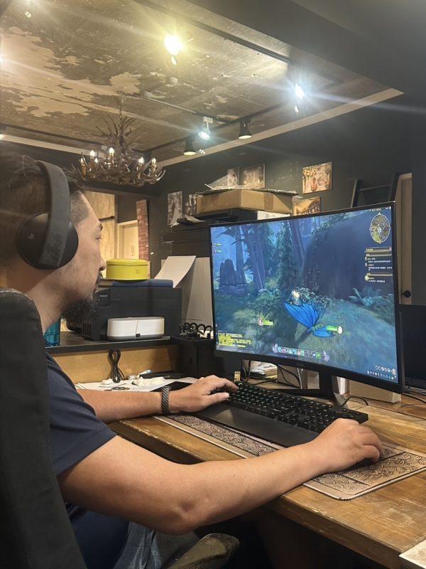 工作者戴耳機於木桌前操作鍵鼠，螢幕顯示森林場景